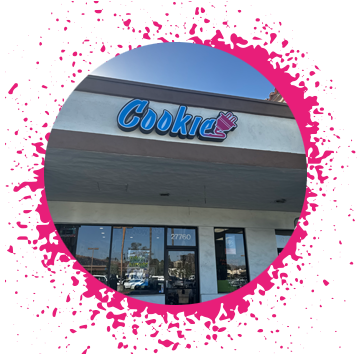 lake forest cookie plug bakery in mission viejo ca Beige storefront with a large blue, purple, and pink gradient sign that says 'Cookie' with an electrical plug attached to the end in graffiti letters over a window sign that says 'Now Hiring'.